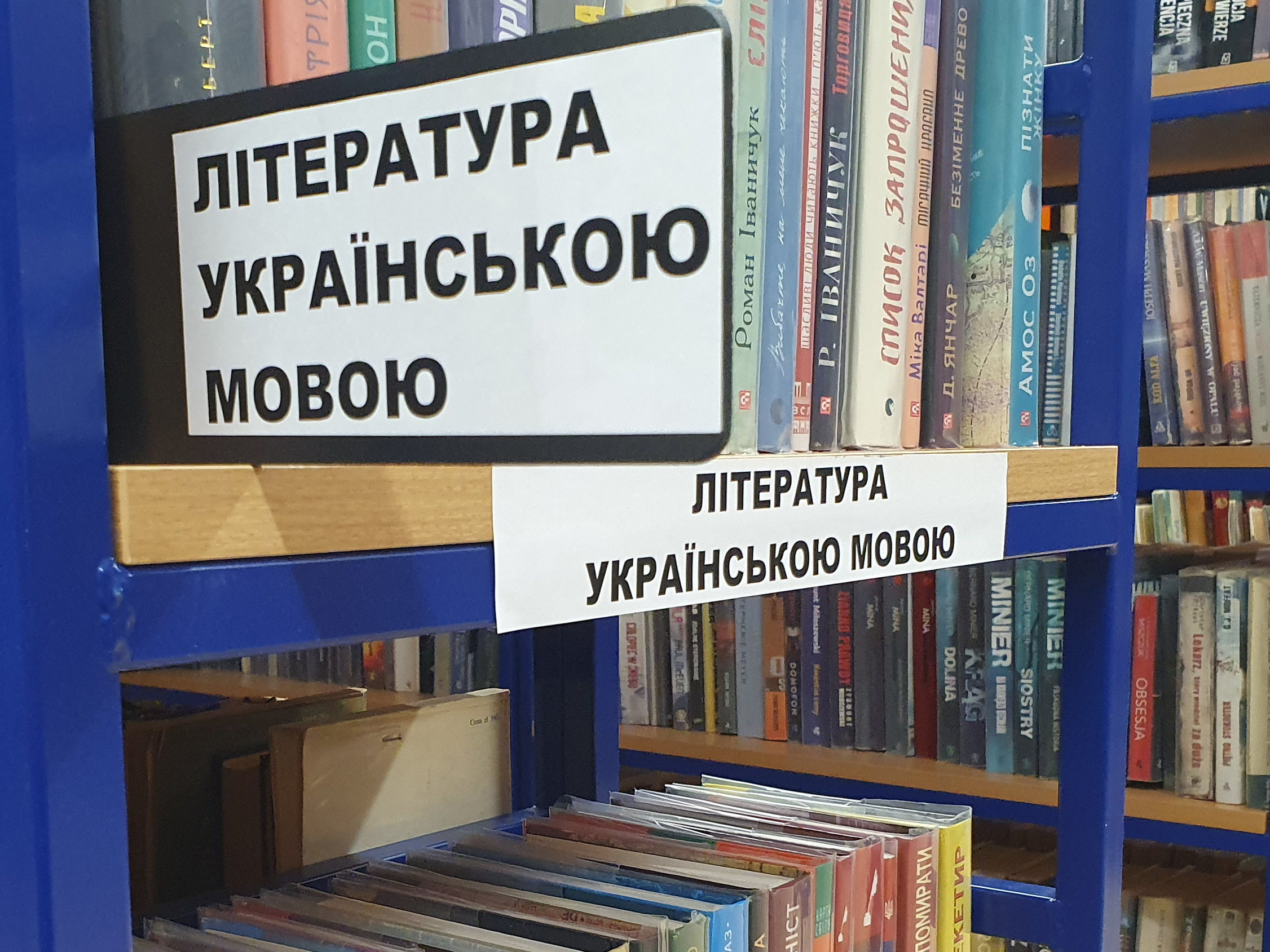 Książki na półkach bibliotecznych. Opatrzone informację w języku ukraińskim pod nazwą "literatura w języku ukraińskim".