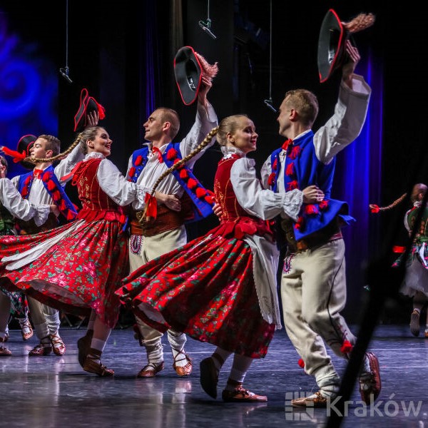 Grupa tancerzy i tancerek w strojach ludowych na scenie.