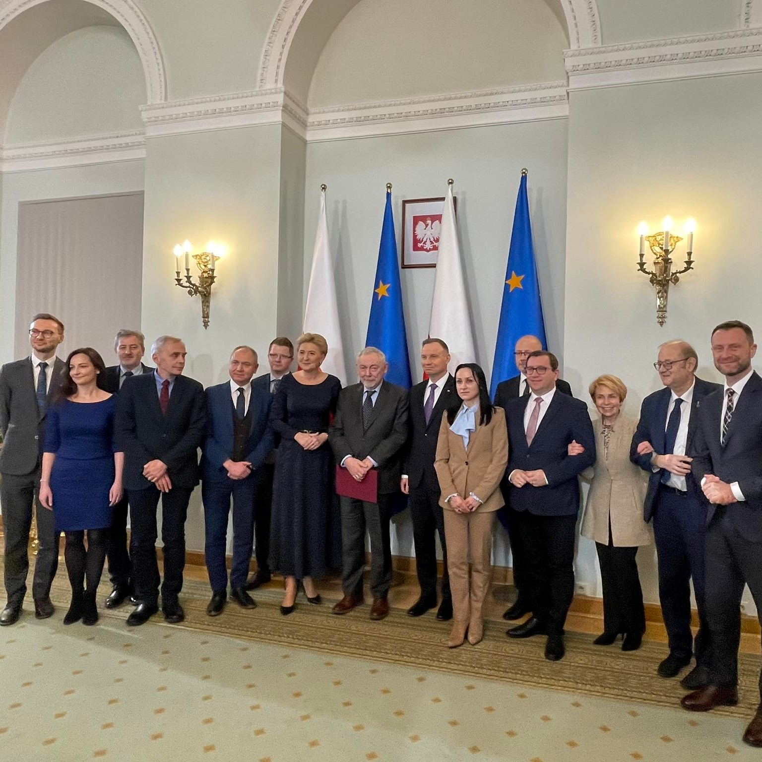 Grupa ludzi pozująca do zdjęcia z Prezydentem RP, w tym dyrektor Ośrodka dr Jarosław Klaś. Na ścianie zawieszono godło Polski i postawiono flagi Polski oraz Unii Europejskiej.